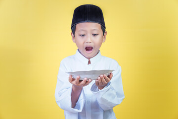 An asian boy looks enthusiastically at the plate in his hand, the concept of Ramdan Kareem...