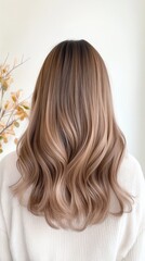 Naklejka premium A person with long, shiny hair is facing away, showcasing natural waves and layers. The smooth texture shines under soft indoor lighting against a plain wall