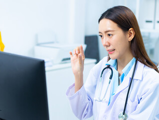 Asian female doctor remotely video call conference, talking with her patient from office. Young asian doctor sits at desk using computer, having online telemedicine, and giving advice to her patient.