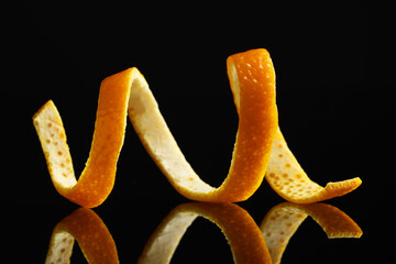 One fresh orange peel on black mirror surface, closeup