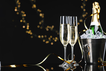 Champagne and bucket of ice on mirror surface against black background with blurred lights, space for text