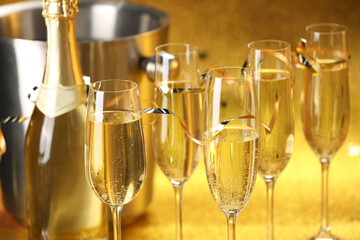 Champagne in glasses, bottle and ice bucket on golden background, closeup