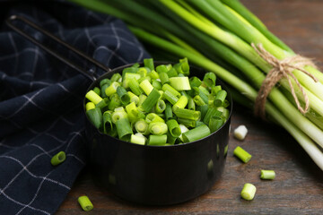 Chopped green onion in saucepan and stems on wooden table, closeup
