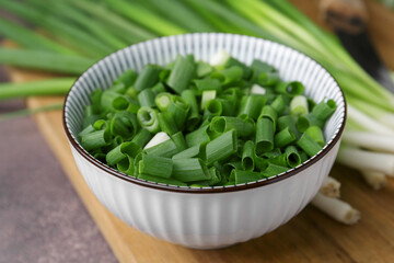 Chopped green onion in bowl and stems on brown table, closeup