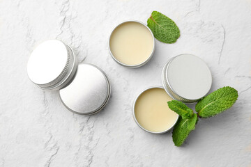 Mint lip balms and green leaves on beige textured background, flat lay. Cosmetic product