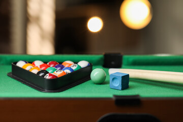 Many colorful billiard balls in triangle rack, cues and chalk on green table indoors, closeup