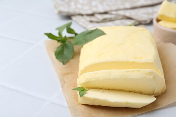 Cut brick of butter and basil on white tiled table, closeup. Space for text