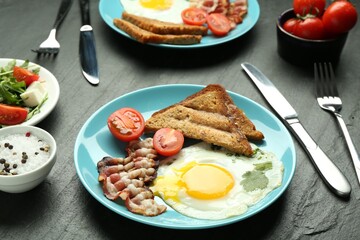Tasty brunch. Delicious fried eggs, bacon, pieces of toast and salad served on black table, closeup