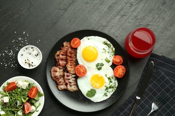 Tasty brunch. Delicious fried eggs, bacon, salad and glass of juice served on black table, flat lay