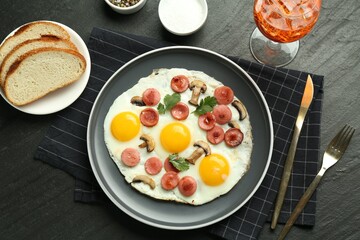 Tasty brunch. Delicious fried eggs with sausage and mushrooms served on black table, flat lay