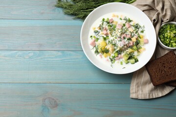 Delicious okroshka soup in bowl on light blue wooden table, flat lay. Space for text