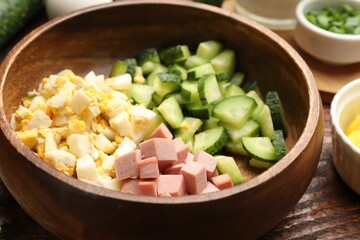 Different ingredients for okroshka soup in bowl on wooden table, closeup
