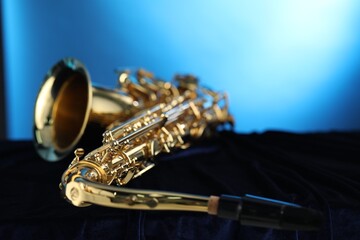 Jazz. One beautiful saxophone on dark fabric against light blue background, closeup. Space for text