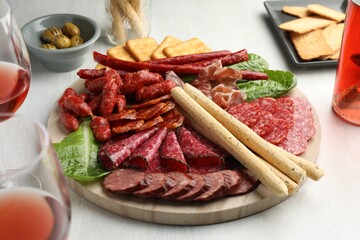 Different smoked sausages and other snacks served with wine on white table, closeup