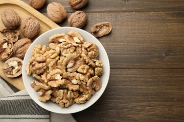 Peeled walnuts in bowl on wooden table, flat lay. Space for text
