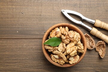 Peeled walnuts in bowl and nutcracker on wooden table, flat lay. Space for text