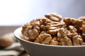 Peeled walnuts in bowl on table against light background, closeup