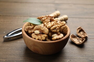 Peeled walnuts in bowl and nutcracker on wooden table, closeup