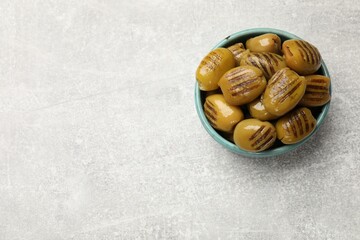 Grilled green olives in bowl on gray textured table, top view. Space for text