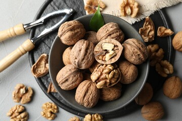 Fresh walnuts in bowl and nutcracker on gray table, flat lay
