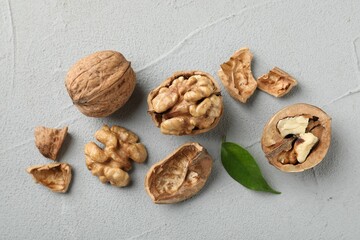 Fresh walnuts with shells and green leaf on gray textured table, flat lay