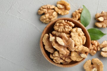 Peeled walnuts in bowl on gray textured table, flat lay. Space for text
