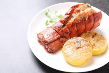 Delicious lobster tail with microgreens and slices of lemon on grey textured table, closeup