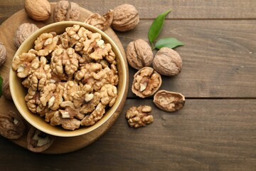 Peeled walnuts in bowl and whole ones on wooden table, flat lay. Space for text