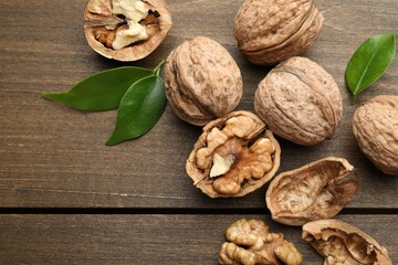 Fresh walnuts and green leaves on wooden table, flat lay. Space for text