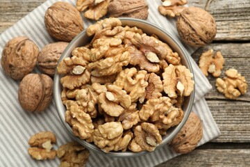 Shelled walnuts in bowl and whole ones on wooden table, flat lay