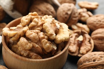 Shelled walnuts in bowl and whole ones on table, closeup