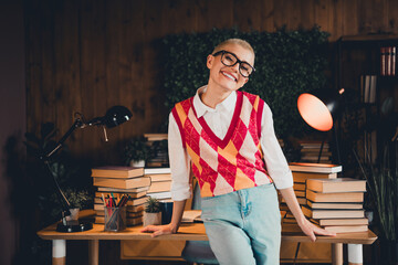 Young woman in a colorful argyle waistcoat smiles at home, surrounded by books and study materials in a cozy room