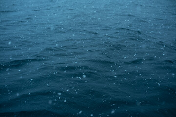 Calm water surface with raindrops creating ripples at twilight