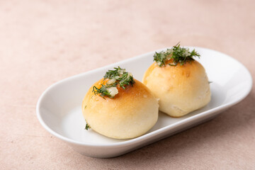 Sweet little buns with garlic and dill on a white plate. Pampushki for breakfast, with borsch or with soup. Traditional homemade baking. Selective focus, close-up.