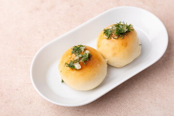 Sweet little buns with garlic and dill on a white plate. Pampushki for breakfast, with borsch or with soup. Traditional homemade baking. Selective focus, close-up.