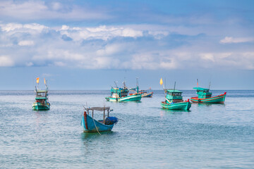 serene coastal scene with several traditional fishing boats floating on calm, turquoise waters. The...