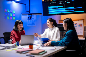 Three women are sitting at a table with laptops and papers