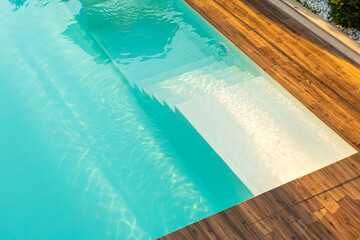 Turquoise swimming pool with elegant submerged steps and wooden deck in a serene outdoor setting