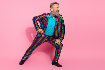 Eccentric elderly gentleman in a colorful suit posing joyfully against a pink background, exuding charismatic and lively energy.