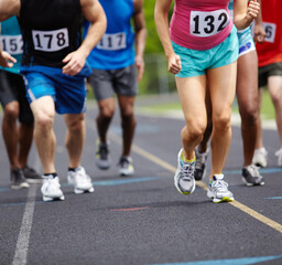 Fitness, legs and group of athletes running on track for race, challenge or marathon with speed. Sports, energy and body of people with energy for cardio workout, exercise or training at stadium.