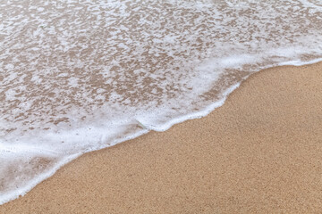 Texture of a wave from the sea with a little white foam slowly advancing a sandy beach