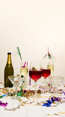 Glasses filled with red and champagne drinks, gold decorations, confetti, and empty bottles scattered on white table, capturing messy afterparty atmosphere. Concept of alcohol, hangover. Ad