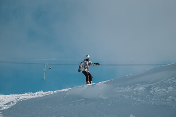 Snowboarder gliding down a snowy hill under a clear blue sky