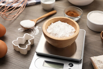 Kitchen scale with bowl of baking powder, eggs, sugar and cocoa on wooden table, closeup