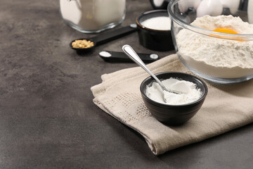 Baking powder and spoon in bowl on grey textured table. Space for text