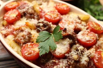 Delicious pasta casserole with cheese, tomatoes, parsley and minced meat in baking dish on table, closeup