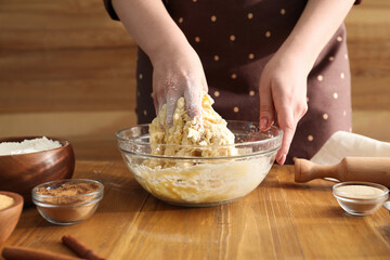 Woman kneading dough for cinnamon rolls at wooden table, closeup