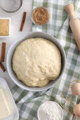 Making cinnamon rolls. Fresh dough in bowl, ingredients and rolling pin on light wooden table, flat lay