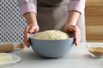 Making cinnamon rolls. Woman with dough at white wooden table, closeup