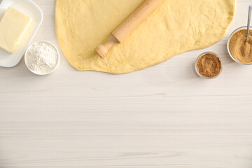 Making cinnamon rolls. Dough, other ingredients and rolling pin on white wooden table, flat lay. Space for text